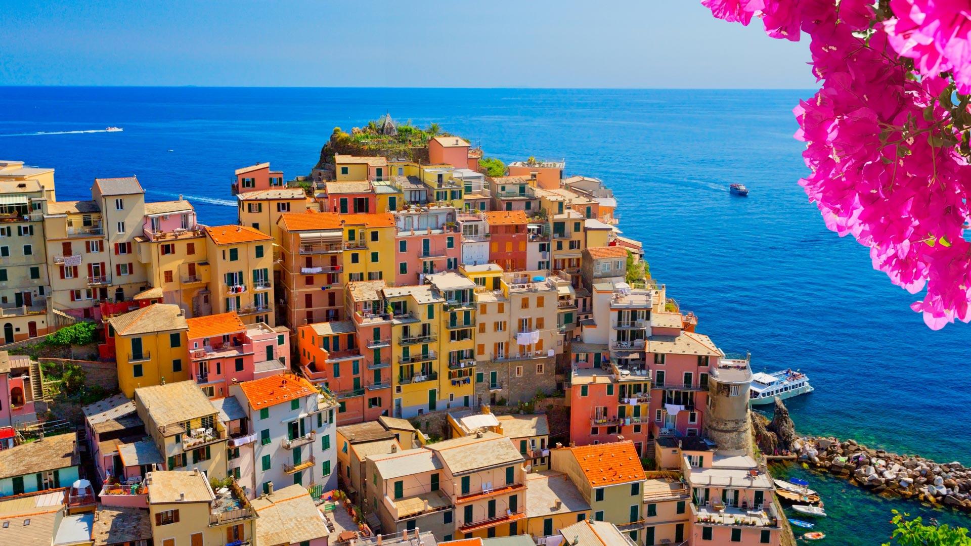 Maisons colorées sur une falaise, mer bleue et fleurs roses.