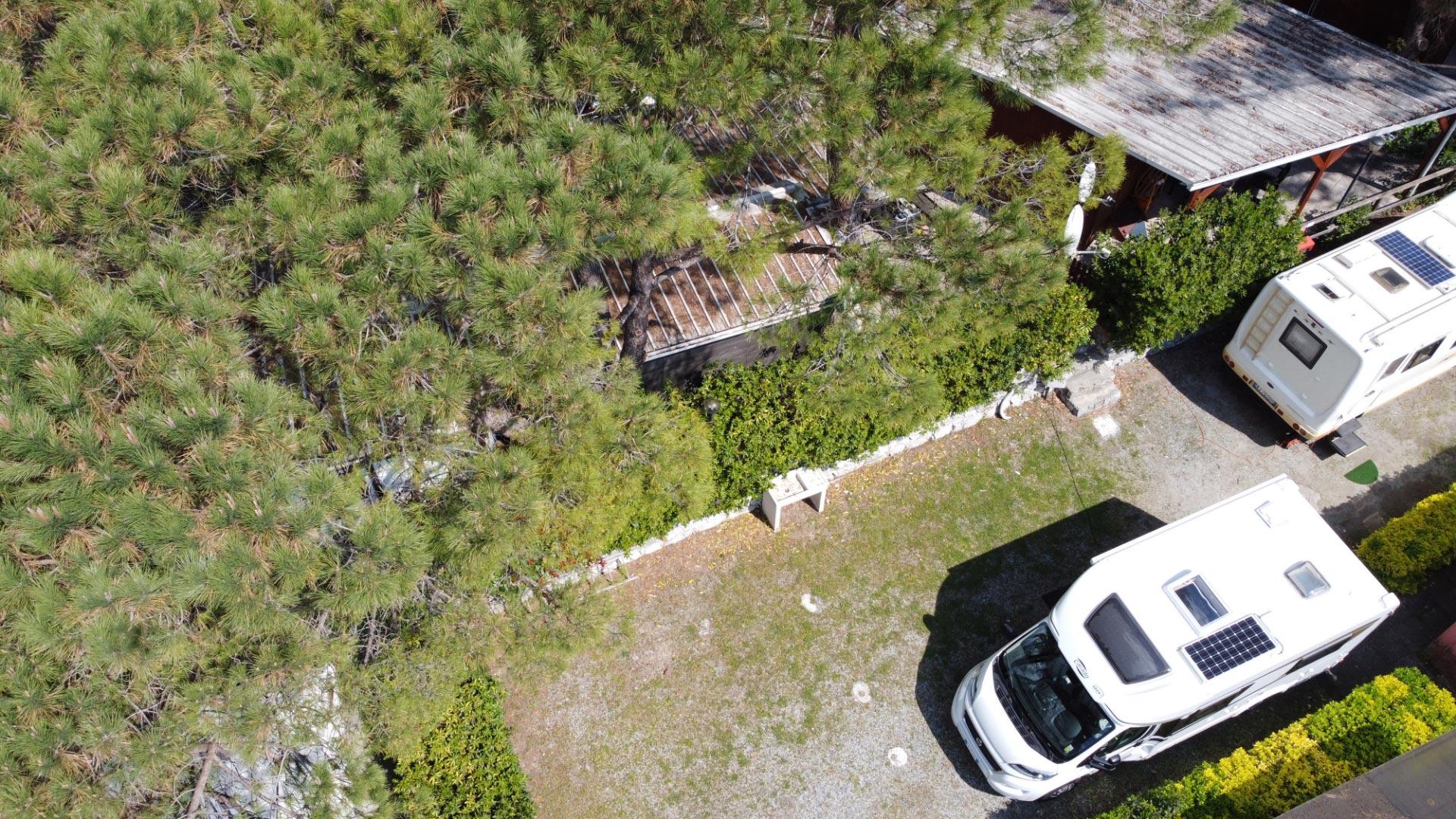 Vue aérienne de camping-cars garés près d'une maison avec des arbres et des buissons.