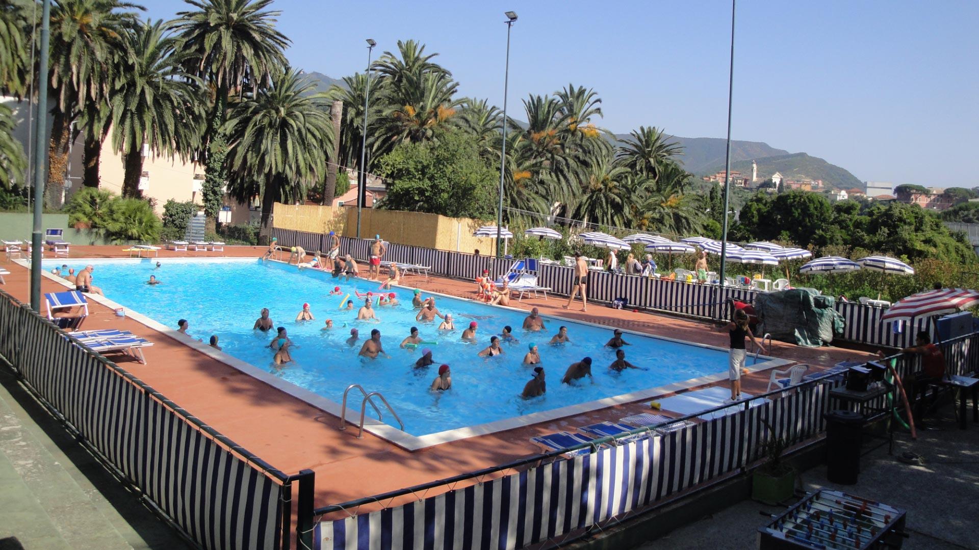 Outdoor pool with people swimming, surrounded by palm trees.