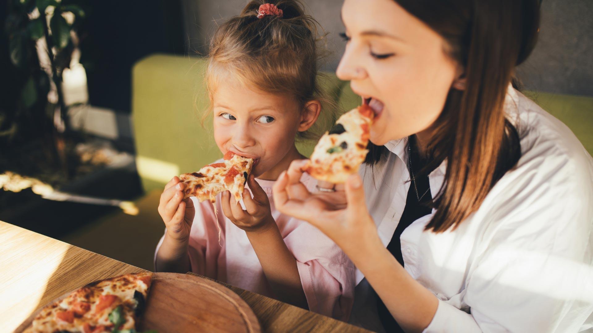 Mother and daughter eating pizza together, smiling and having fun.