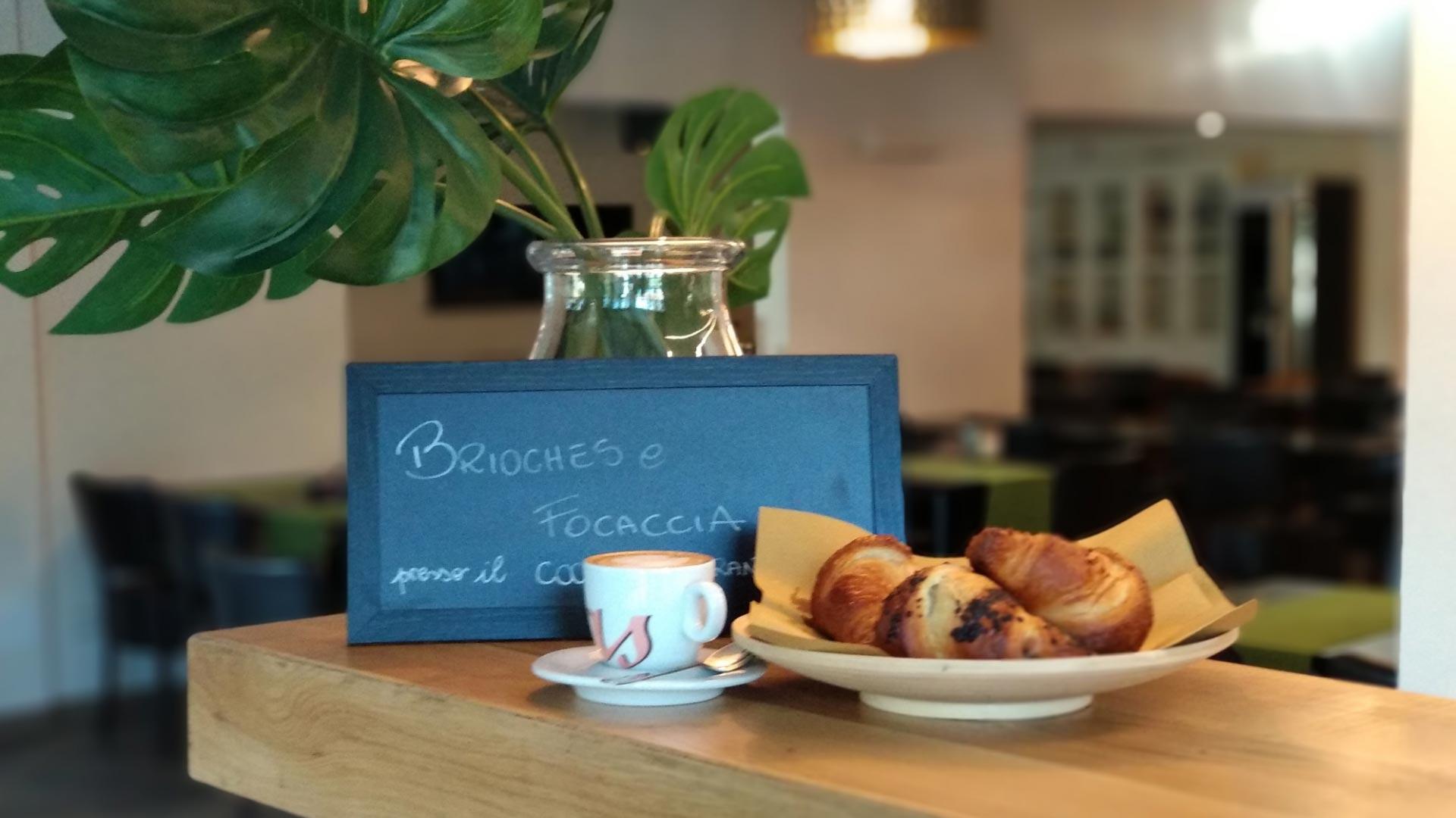 Coffee and croissants on a table with a chalkboard and decorative plant.