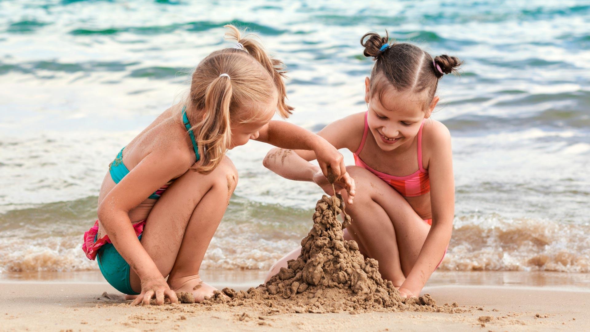 Zwei Mädchen spielen am Strand und bauen eine Sandburg.