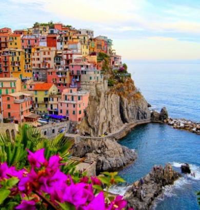 Colorful houses on a cliff with sea view and flowers in the foreground.