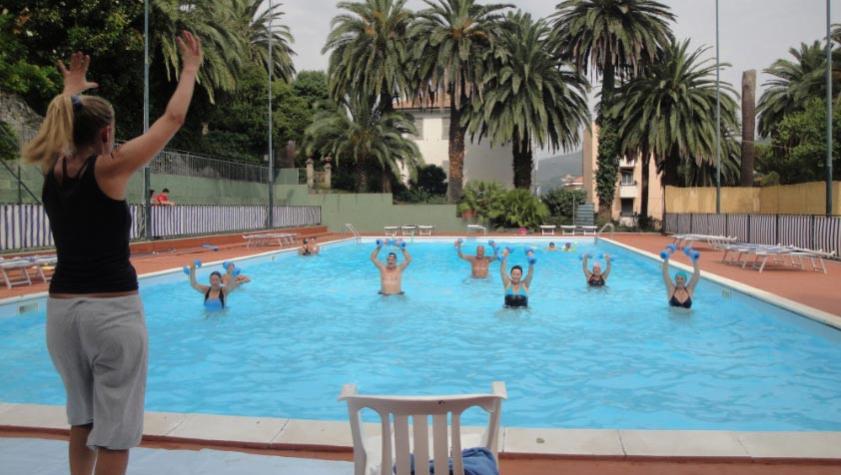 Water aerobics class in a pool with instructor, palm trees in the background.