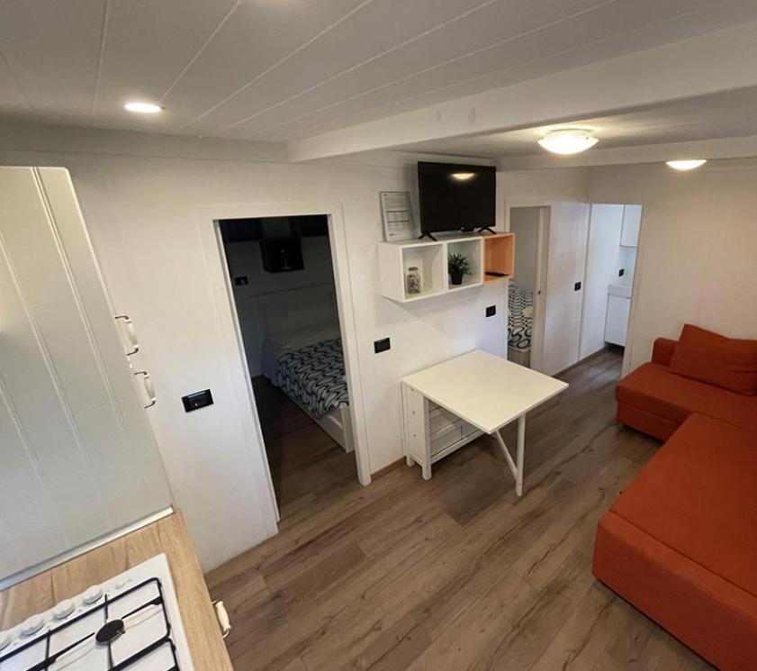 Salon moderne avec canapé orange, cuisine et chambre.