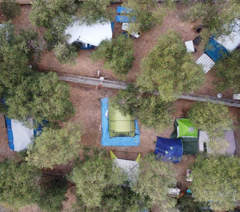 Vista dall'alto di un campeggio tra gli alberi con diverse tende colorate.