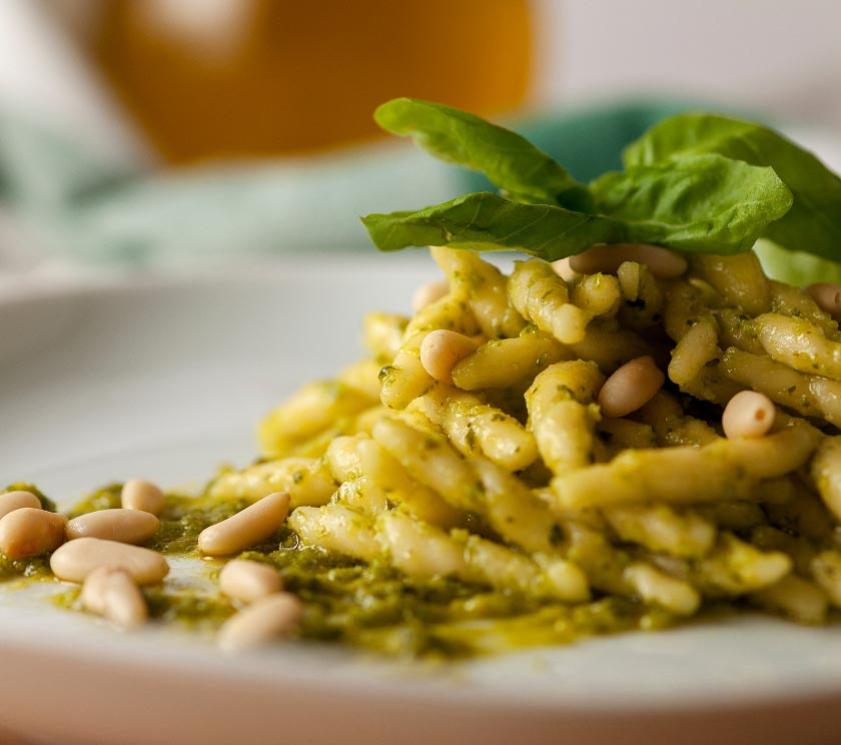 Pasta with pesto, pine nuts, and fresh basil leaves.