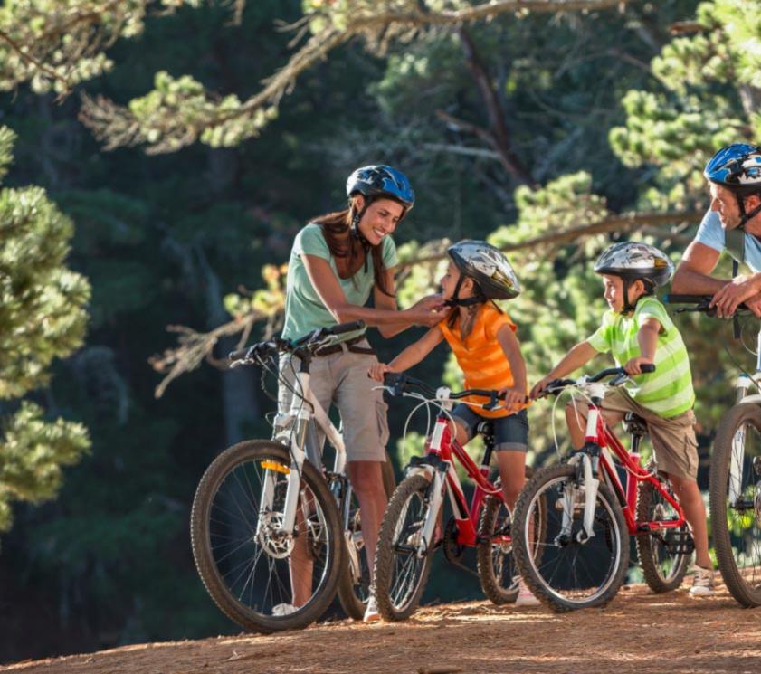 Family biking in the woods, wearing protective helmets.