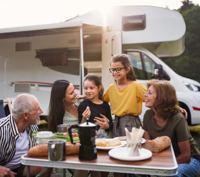 Happy family camping with an RV, enjoying an outdoor meal.