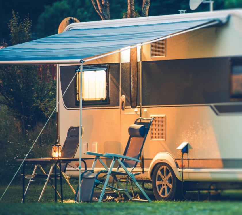 Camper with awning, chairs, and table lit up in the evening.