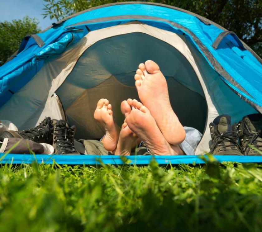 Two people relaxing in a camping tent with shoes outside.