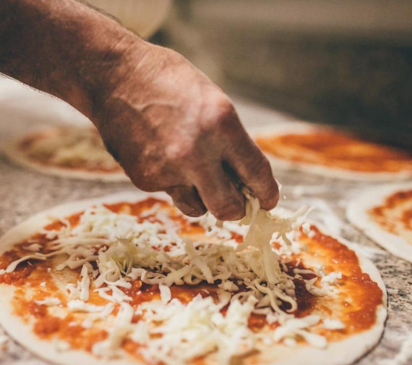 Hand fügt Käse auf Pizza mit Tomatensauce hinzu.