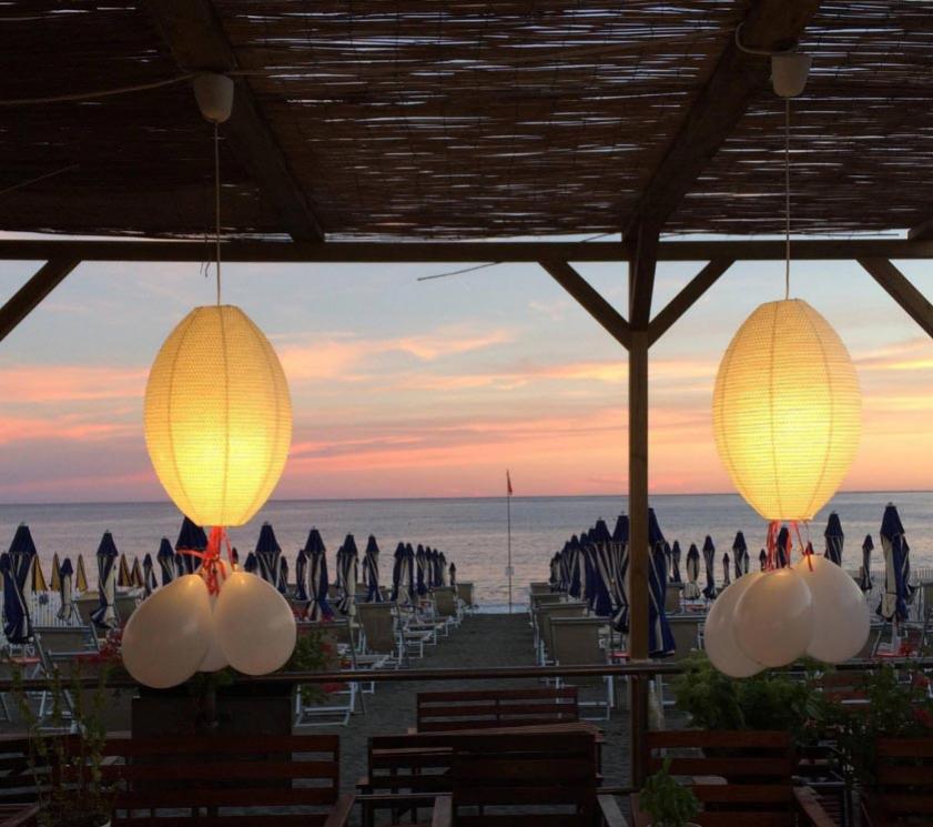 Strand bei Sonnenuntergang mit beleuchteten Laternen und geschlossenen Schirmen.