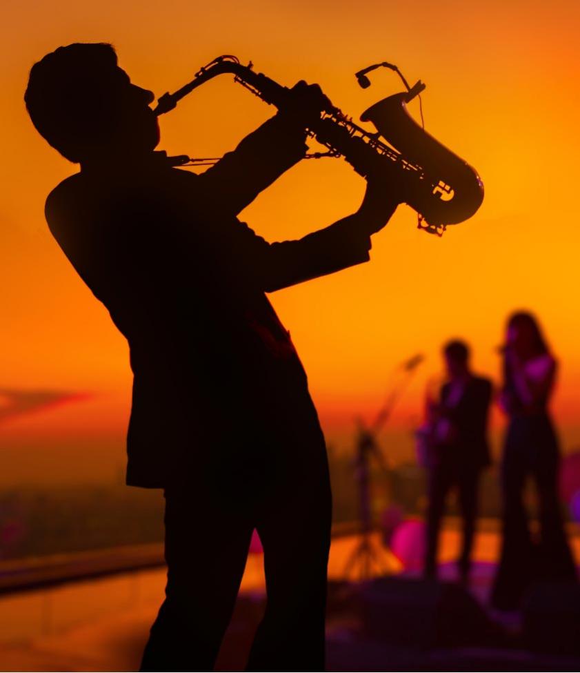 Silhouette of a saxophonist at sunset with a band in the background.